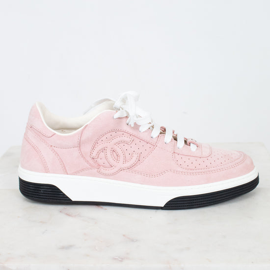 A light pink Chanel low-top sneaker with white laces, a white midsole, and a black outsole, displayed on a white marble surface against a white background.
