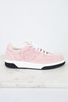 A light pink Chanel low-top sneaker with white laces, a white midsole, and a black outsole, displayed on a white marble surface against a white background.