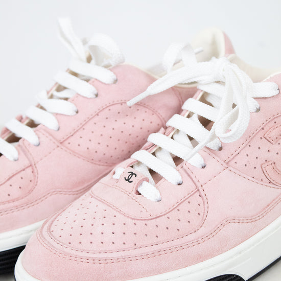 A pair of low-top pink sneakers with white laces, a white midsole, and a black rubber outsole. One shoe shows a small interlocking CC logo on the side, indicating they are Chanel brand.