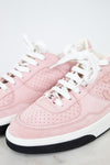 A pair of low-top pink sneakers with white laces, a white midsole, and a black rubber outsole. One shoe shows a small interlocking CC logo on the side, indicating they are Chanel brand.