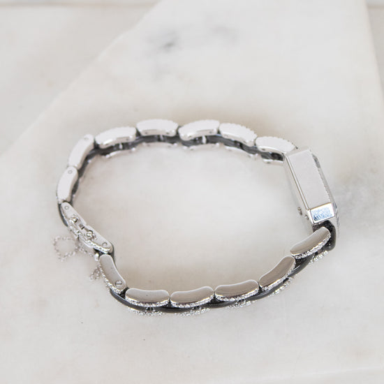 A silver-toned segmented bracelet with a polished rectangular clasp, displayed on a white marble surface.