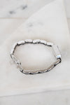 A silver-toned segmented bracelet with a polished rectangular clasp, displayed on a white marble surface.