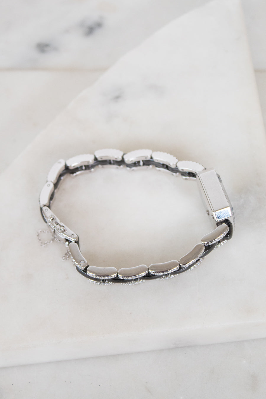 A silver-toned segmented bracelet with a polished rectangular clasp, displayed on a white marble surface.