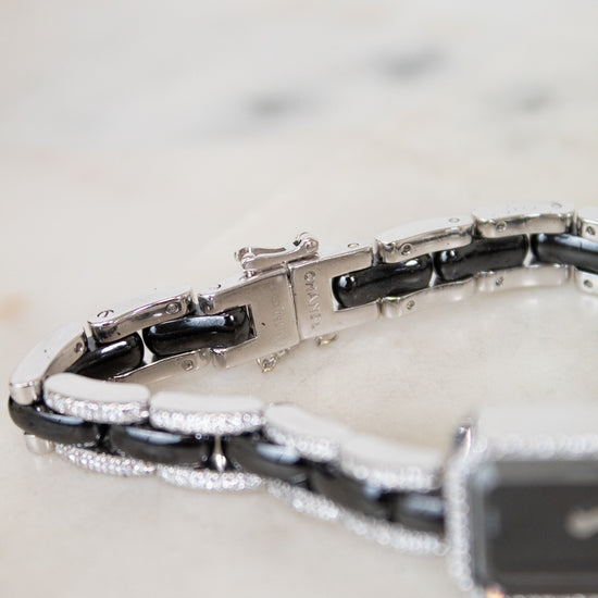 A close-up of a bracelet with alternating glossy black and polished silver links, accented with small diamonds, resting on a light marble surface.