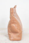 A tan quilted leather shoulder bag shown from a side profile view, resting on a light marble surface against a white background.
