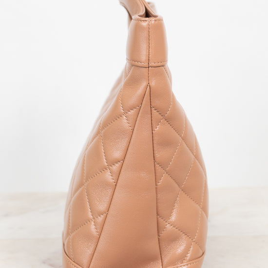 A tan quilted leather shoulder bag shown from a side profile view, resting on a light marble surface against a white background.