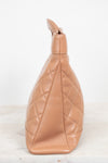 A tan quilted leather shoulder bag shown from a side profile view, resting on a light marble surface against a white background.
