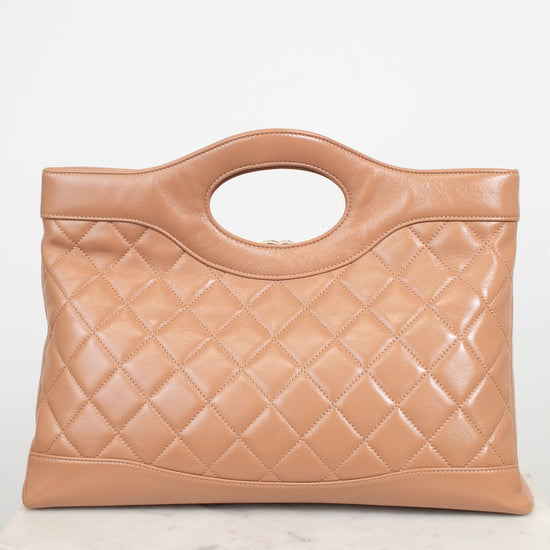 A tan quilted leather handbag with a top handle, displayed on a light marble surface against a white background.