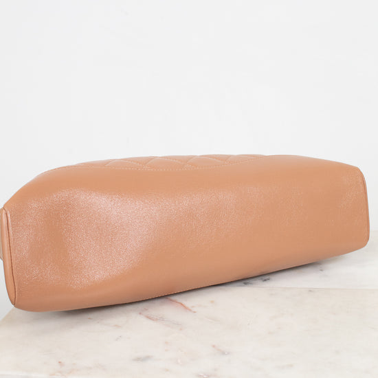 A tan lambskin leather clutch bag with a rounded rectangular shape, resting on a white marble surface against a white background.