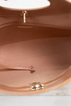 Close-up of the interior of a tan leather handbag, showing the lining, zipper track, and gold-tone hardware against a light surface.