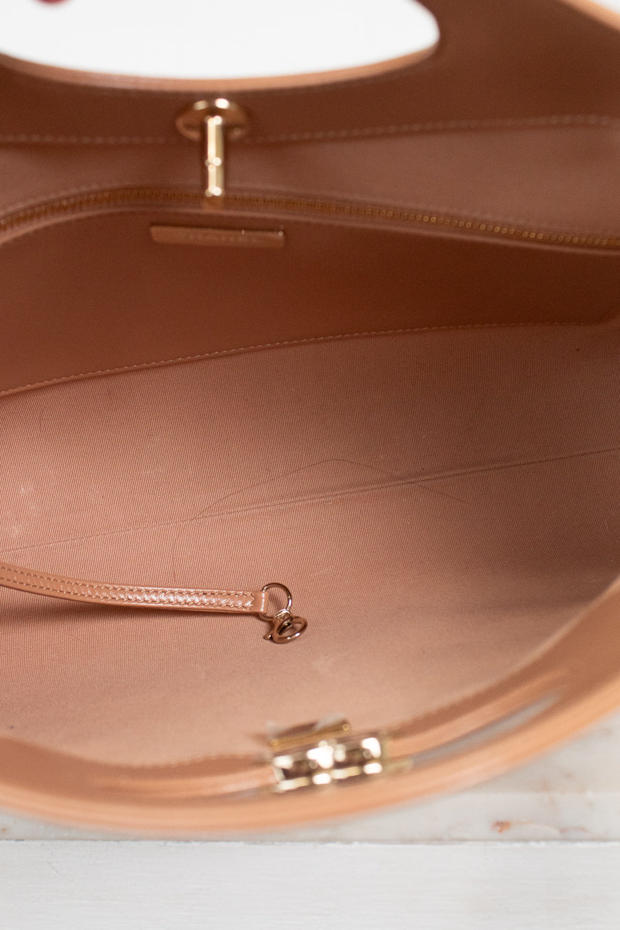 Close-up of the interior of a tan leather handbag, showing the lining, zipper track, and gold-tone hardware against a light surface.