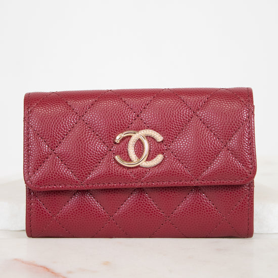 A red quilted leather wallet with a gold-tone interlocking CC logo on the front, resting on a light marble surface against a white background.