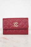 A red quilted leather wallet with a gold-tone interlocking CC logo on the front, resting on a light marble surface against a white background.
