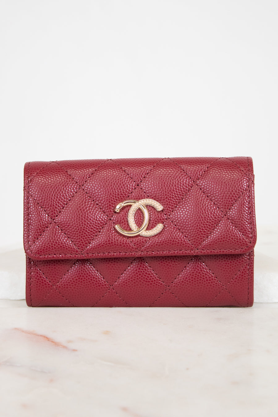 A red quilted leather wallet with a gold-tone interlocking CC logo on the front, resting on a light marble surface against a white background.