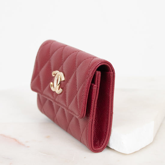 A red quilted leather wallet with a gold-tone interlocking CC logo, resting on a white marble block against a white background.