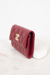 A red quilted leather wallet with a gold-tone interlocking CC logo, resting on a white marble block against a white background.