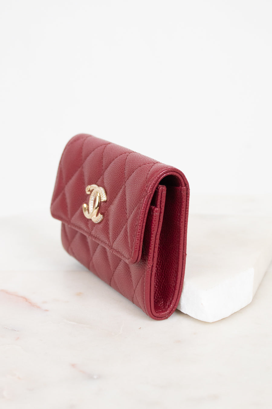 A red quilted leather wallet with a gold-tone interlocking CC logo, resting on a white marble block against a white background.