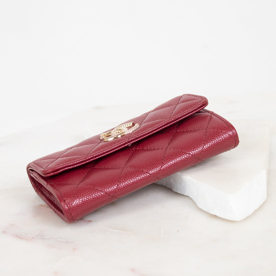 A burgundy quilted leather wallet with a gold-tone interlocking CC logo clasp, resting on a white marble block against a white background.