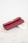 A burgundy quilted leather wallet with a gold-tone interlocking CC logo clasp, resting on a white marble block against a white background.