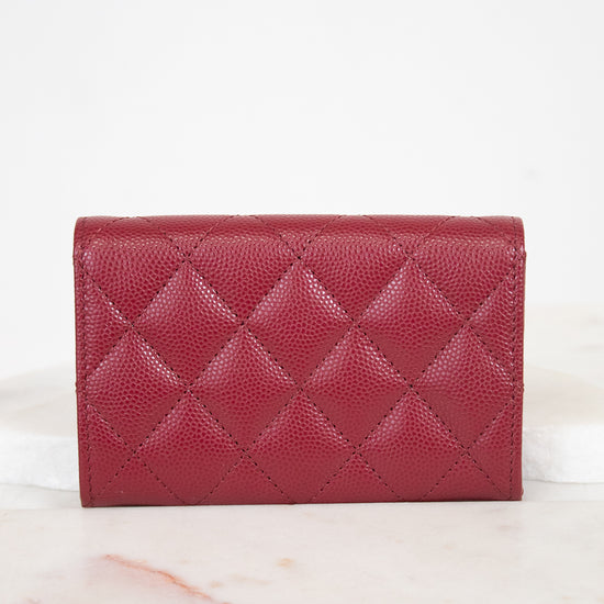 A red quilted leather wallet with a pebbled texture, displayed on a white marble surface against a white background.