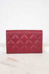 A red quilted leather wallet with a pebbled texture, displayed on a white marble surface against a white background.