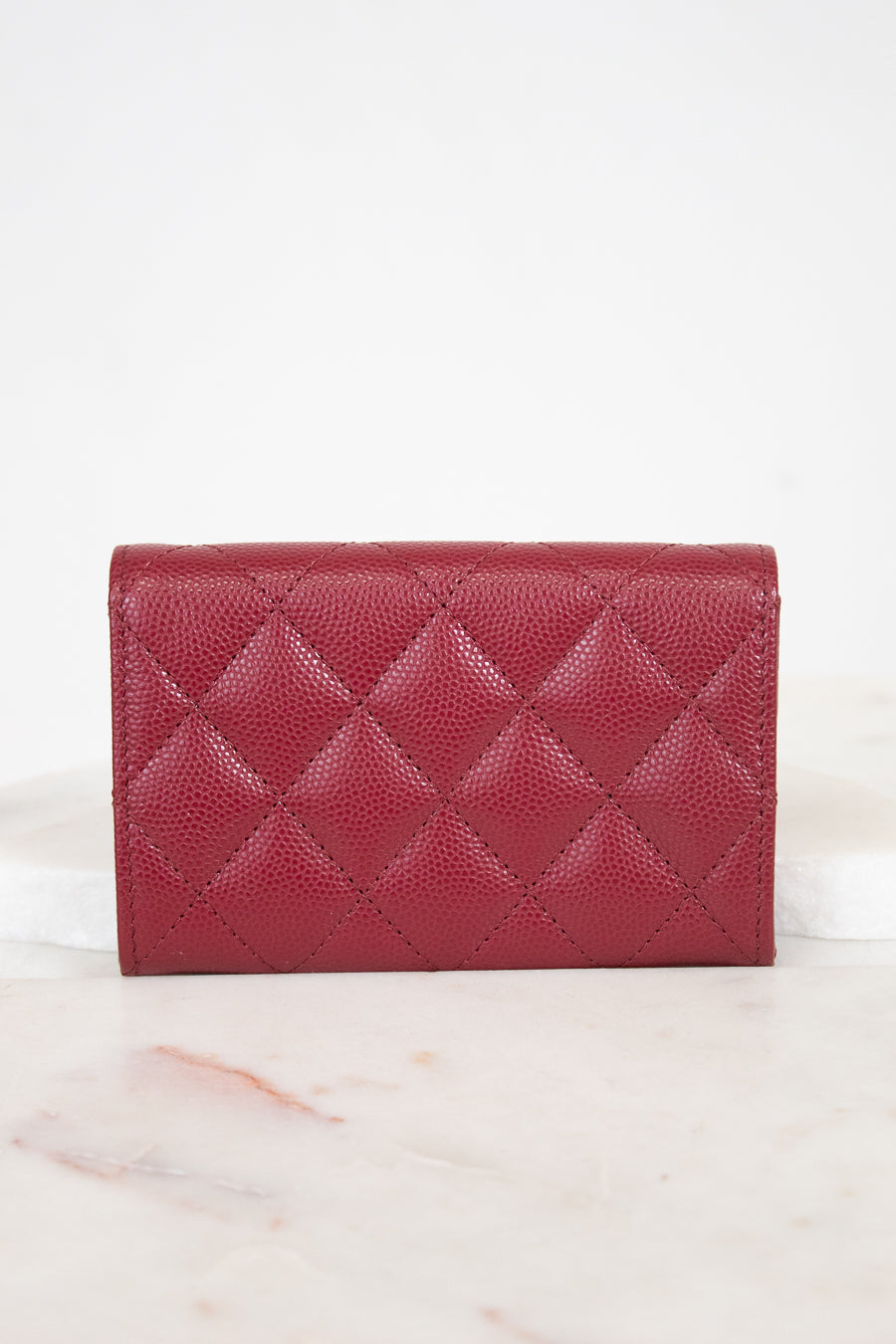 A red quilted leather wallet with a pebbled texture, displayed on a white marble surface against a white background.