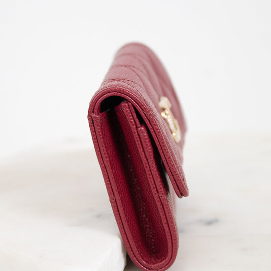 A close-up side view of a burgundy textured leather wallet resting on a white marble block against a white background.