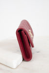 A close-up side view of a burgundy textured leather wallet resting on a white marble block against a white background.
