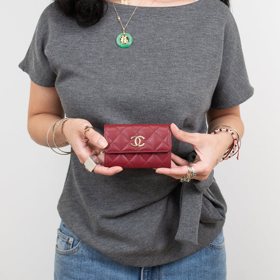A woman wearing a gray t-shirt and blue jeans holds a small red quilted Chanel wallet with a gold CC logo.