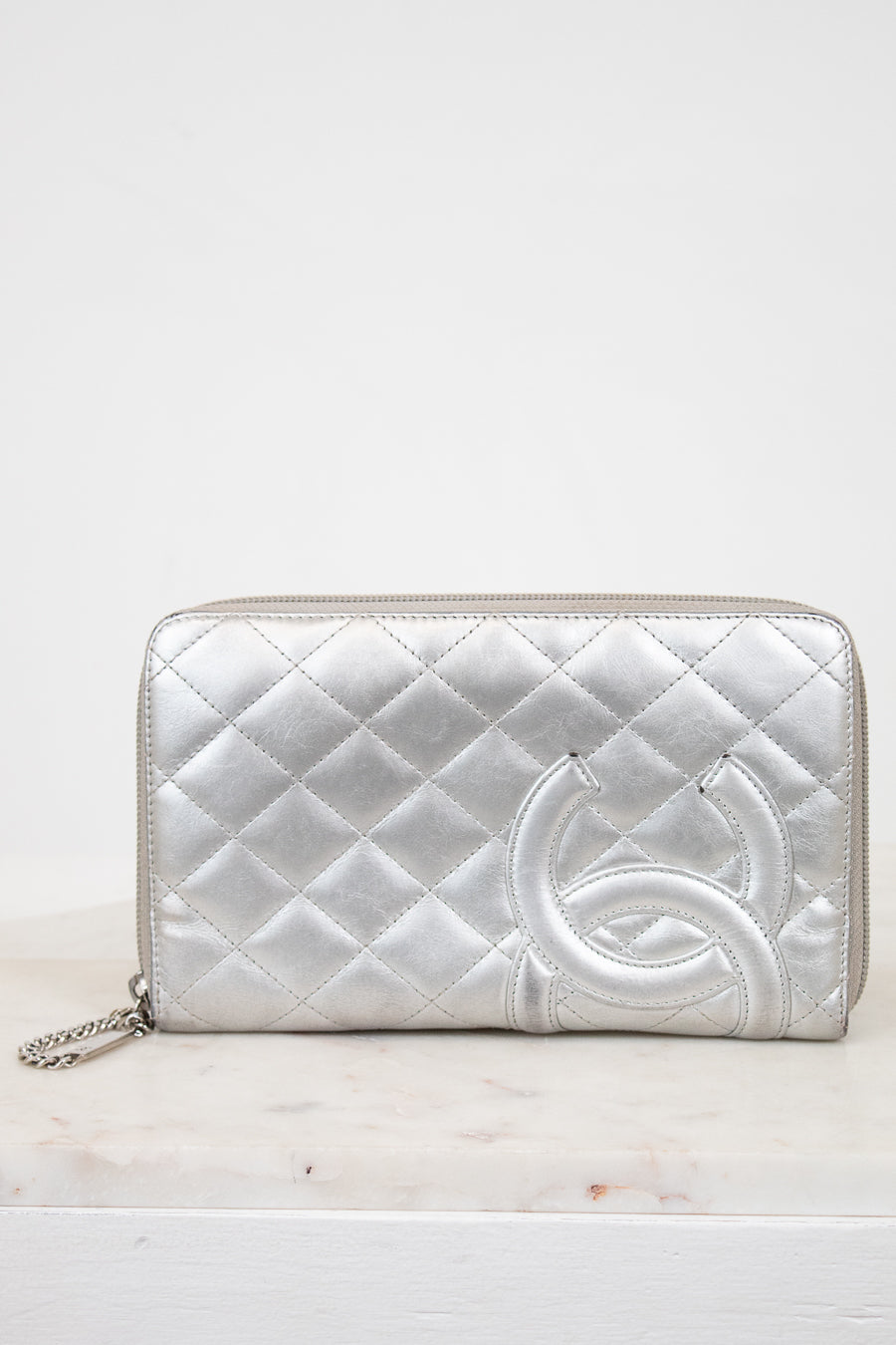 Silver quilted wallet with a brand logo on a white background