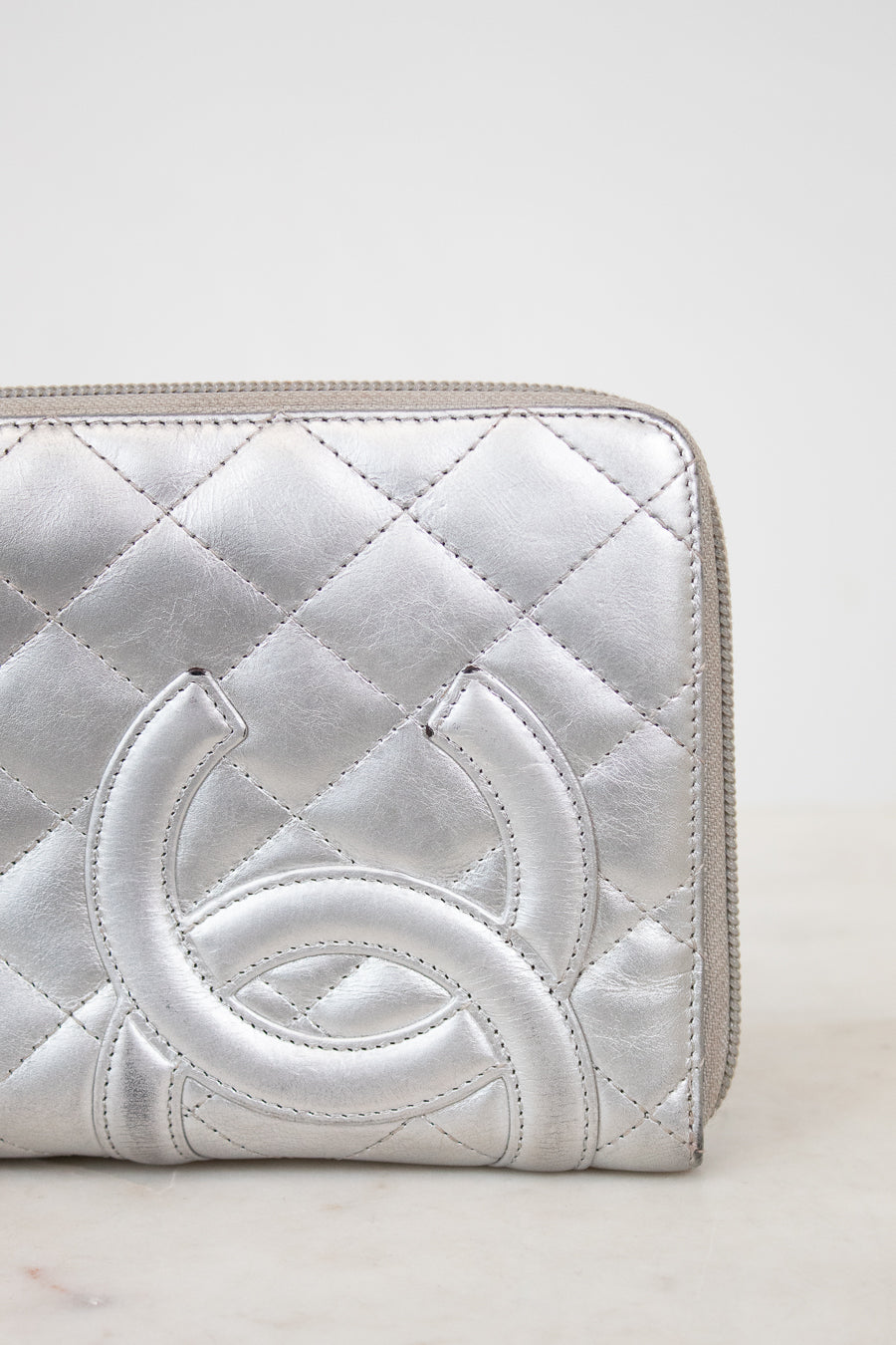 Silver quilted wallet with a brand logo on a white background