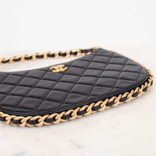 A close-up of a black quilted leather handbag with a gold chain strap and a gold interlocking CC logo, resting on a white marble surface.