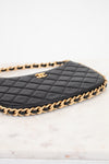 A close-up of a black quilted leather handbag with a gold chain strap and a gold interlocking CC logo, resting on a white marble surface.