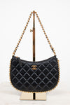 A black quilted leather shoulder bag with a gold-tone chain strap and a gold interlocking CC logo, displayed on a gold stand against a white background.
