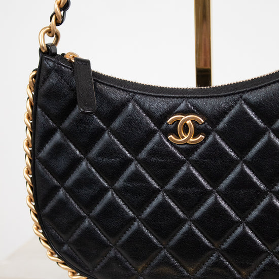 A black quilted leather shoulder bag with a gold-tone interlocking CC logo, displayed on a stand against a white background.