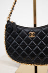 A black quilted leather shoulder bag with a gold-tone interlocking CC logo, displayed on a stand against a white background.