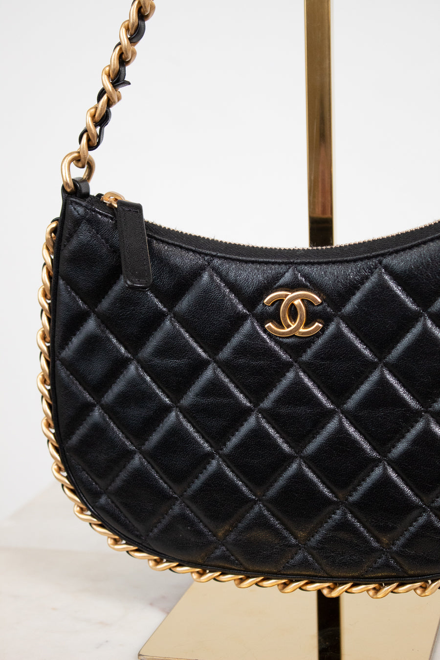 A black quilted leather shoulder bag with a gold-tone interlocking CC logo, displayed on a stand against a white background.