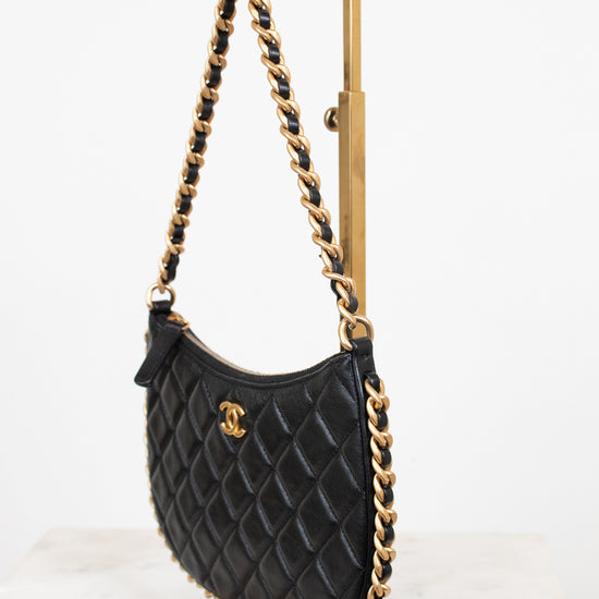 A black quilted leather shoulder bag with gold-tone chain strap and a gold interlocking CC logo, displayed on a gold stand against a white background.