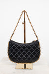 A black quilted leather shoulder bag with gold-tone chain straps, displayed on a gold metal stand against a white background.