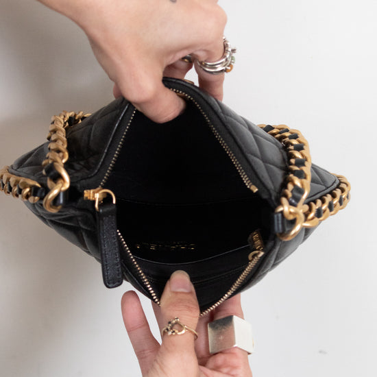 A close-up of a black quilted leather handbag with gold-tone chain straps, held open by two hands against a plain white background.