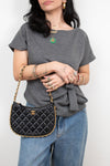 A woman wearing a gray t-shirt and blue jeans carries a black quilted Chanel shoulder bag with gold hardware and a gold chain strap.