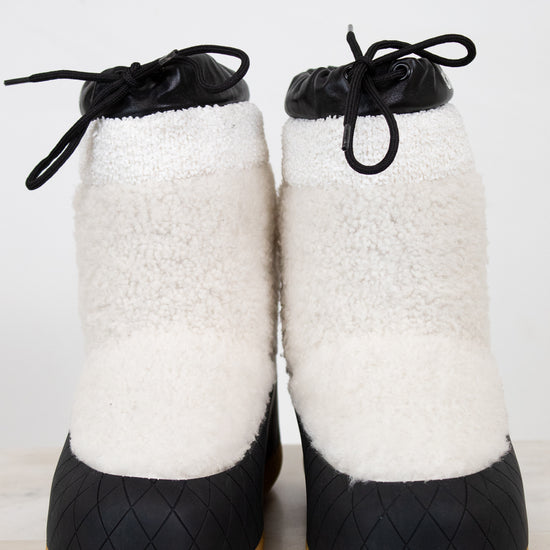 Pair of white fuzzy snow boots with black details on white background.