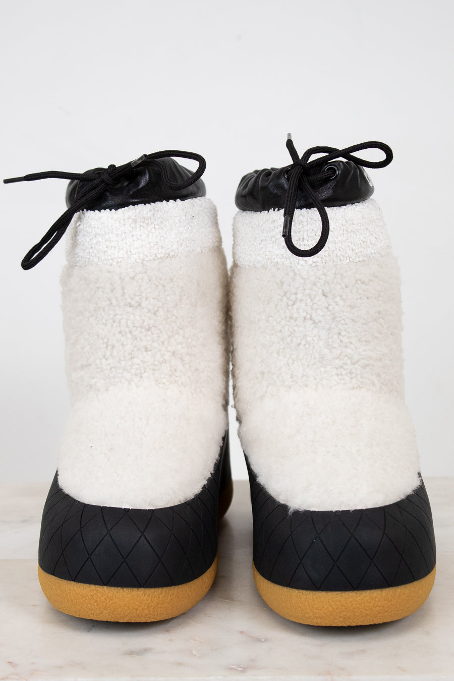 Pair of white fuzzy snow boots with black details on white background.