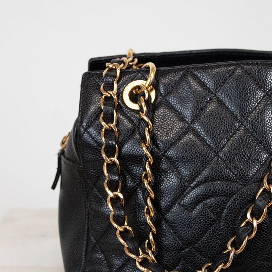 Black quilted handbag with a gold chain on a light gray background