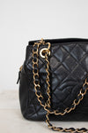 Black quilted handbag with a gold chain on a light gray background