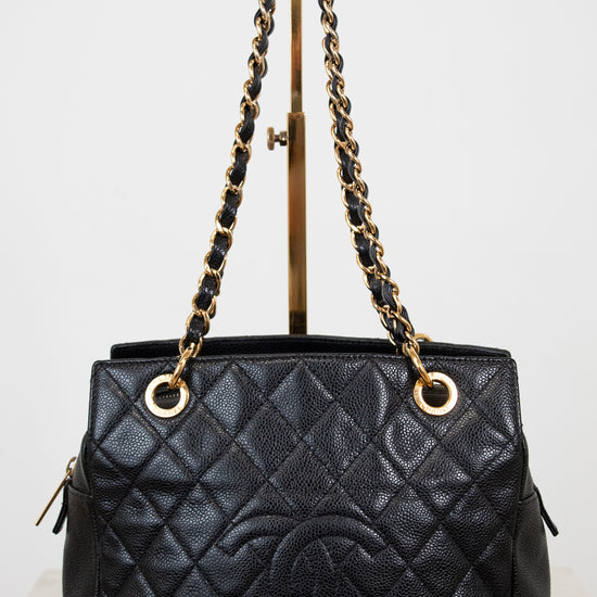 Black quilted handbag with gold chain handle on a stand against a white background