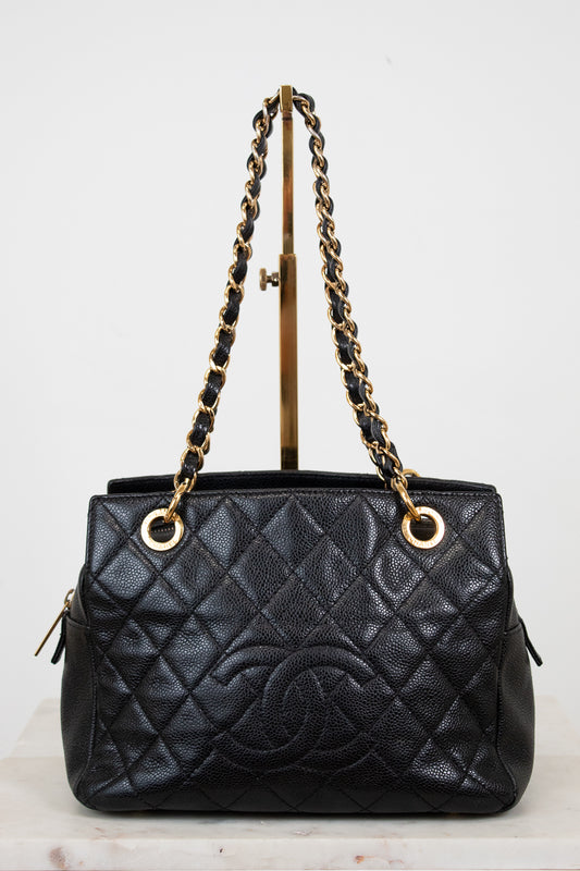 Black quilted handbag with gold chain handle on a stand against a white background