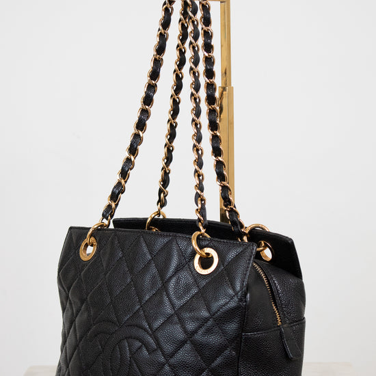 Black quilted handbag with gold chain straps on a white background