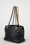 Black quilted handbag with gold chain straps on a white background