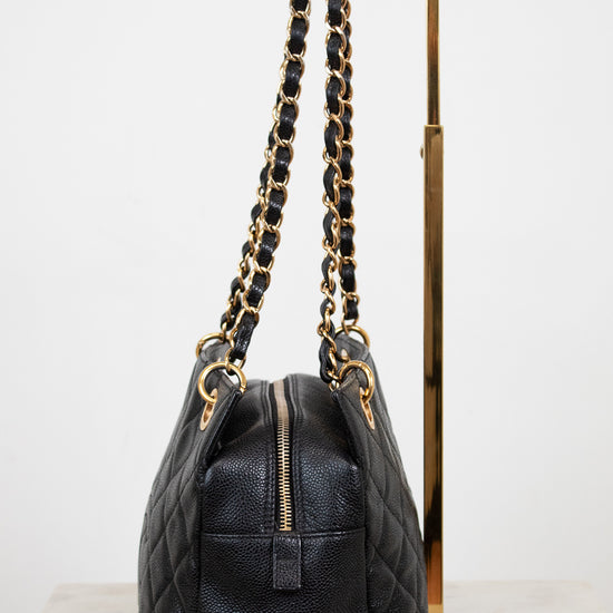 Black quilted handbag with gold chain strap on a white background